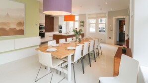 Un comedor moderno con una mesa de madera, sillas blancas y una lámpara colgante morada.