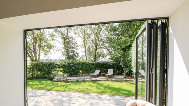 A modern room with a sliding glass door leading to a patio with a lawn, chairs, and a table.