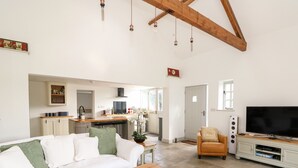 A spacious living area with a white sofa, a wooden coffee table, a TV, and a kitchen in the background.