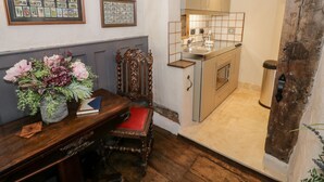 Una cucina compatta con forno a incasso, lavello e una sedia di legno con cuscino rosso. Sopra la sedia, sulla parete, ci sono quadri incorniciati.