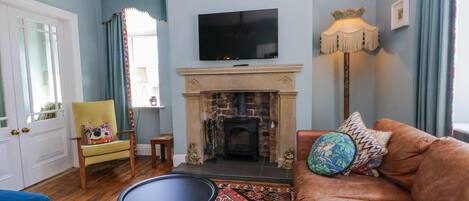 A living room with a fireplace, a television mounted above it, a sofa with decorative pillows, a small round table, and a patterned rug.