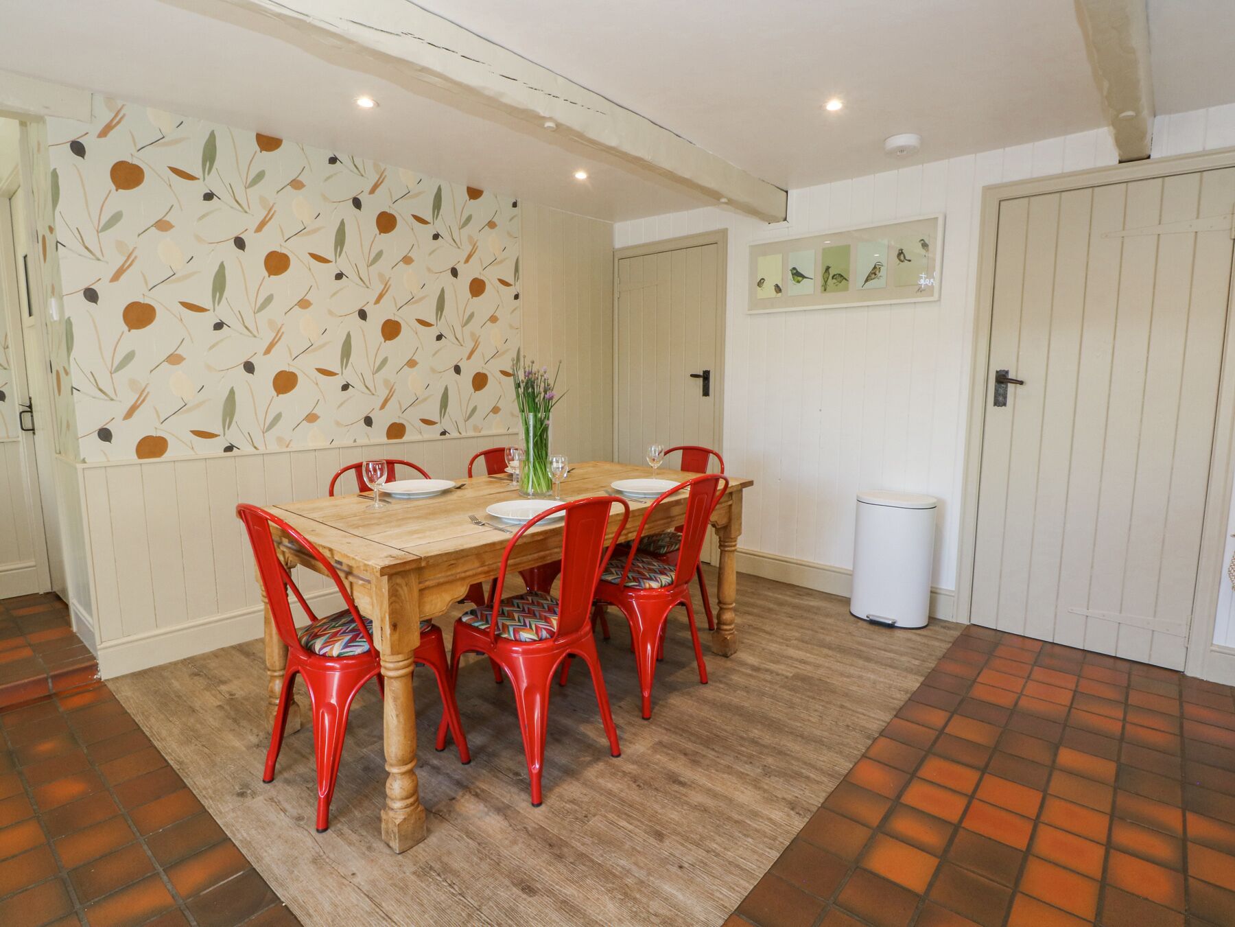 Un comedor con mesa de madera, sillas rojas y un papel tapiz estampado.