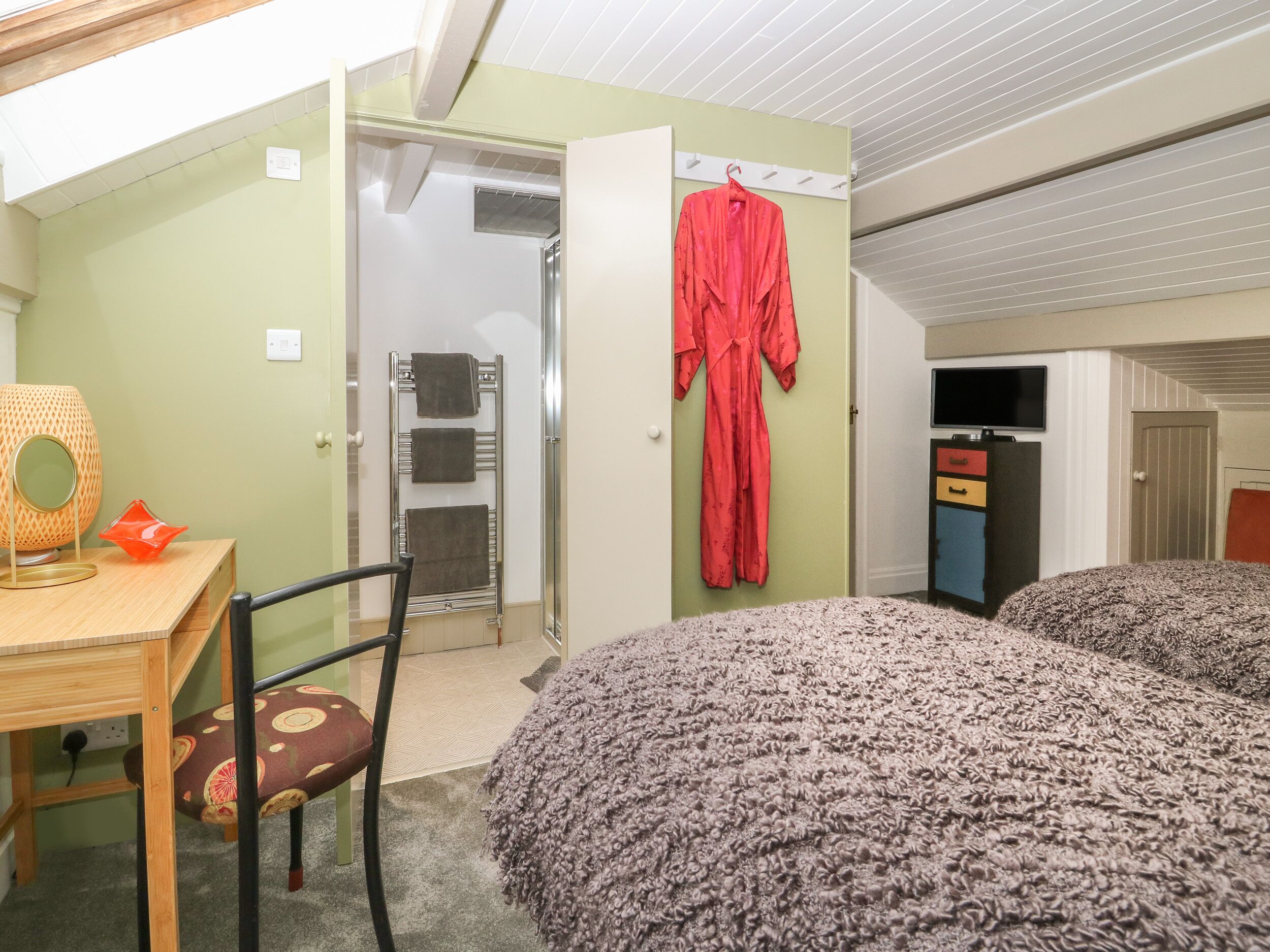 A bedroom with a bed, a desk, a chair, a robe hanging on the wall, and a wardrobe.