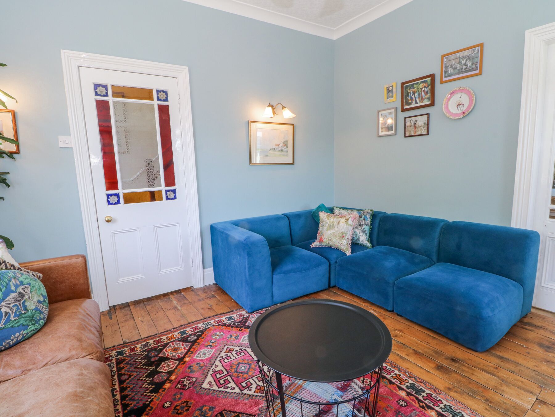 A living room with a blue sofa, a patterned rug, a small round table, and a door with decorative glass panels.