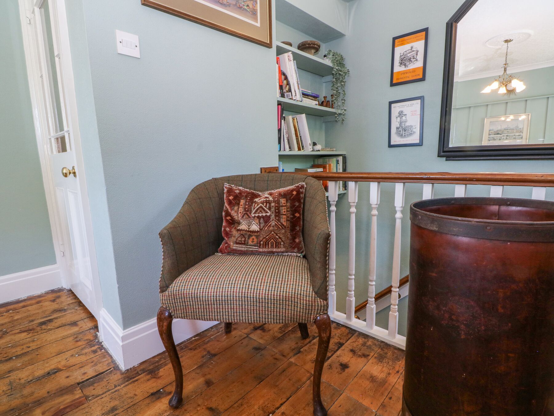 A room with a wooden floor, a chair with a patterned cushion, a bookshelf, and a large copper pot.