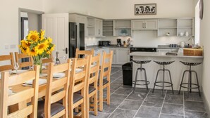 Una cocina moderna con armarios blancos, un refrigerador negro y un comedor con sillas de madera y un jarrón de girasoles.