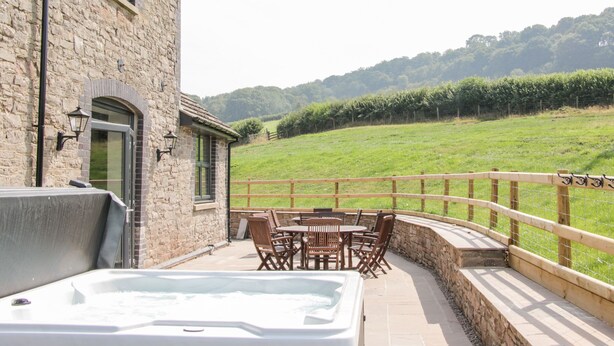 Un edificio de piedra con jacuzzi y zona de estar exterior con vistas a un campo verde.