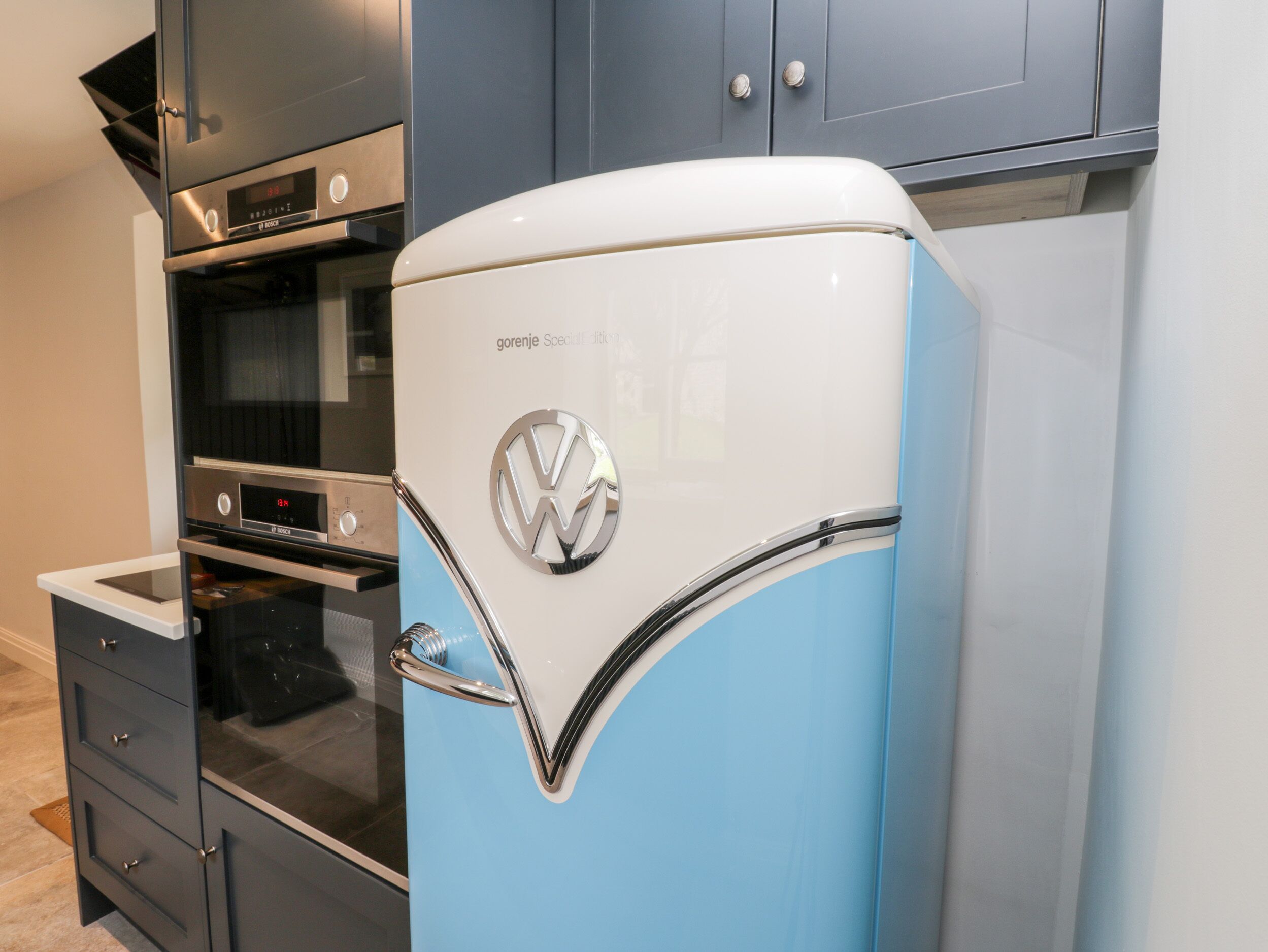 A kitchen with a vintage blue refrigerator, a modern oven, and dark cabinetry.
