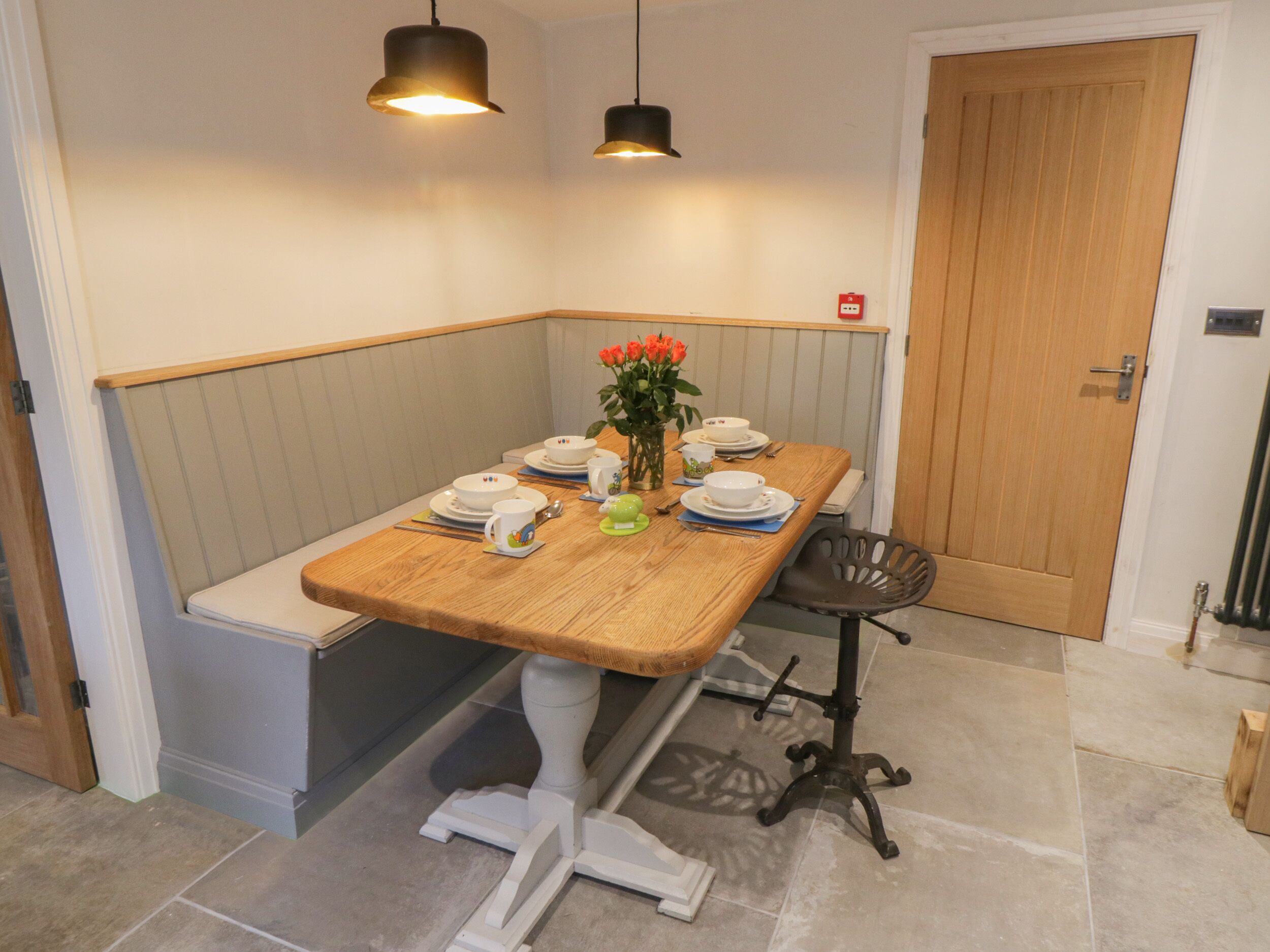 A corner dining area with a wooden table set for four, a bench, and two pendant lights.