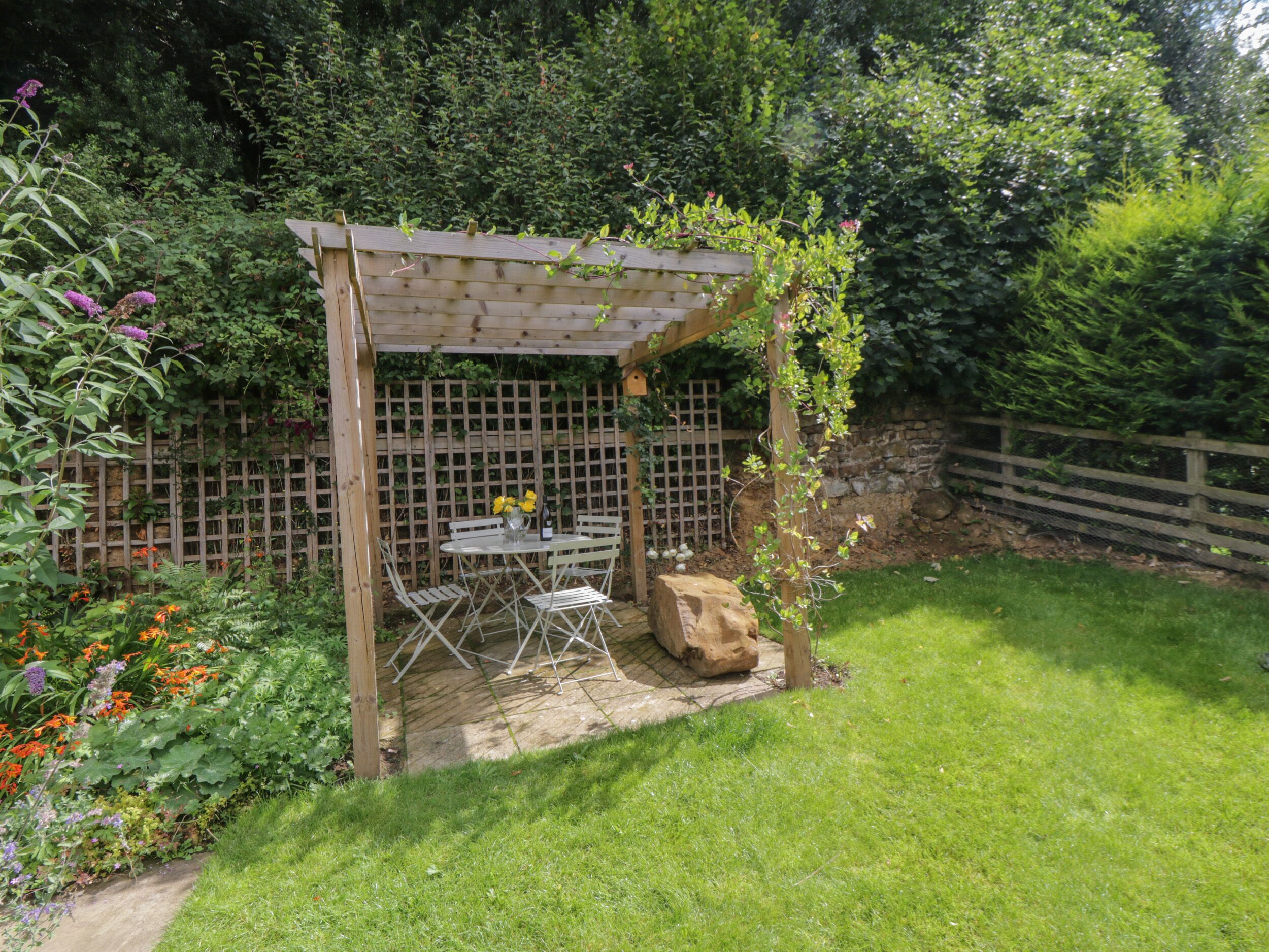 A wooden pergola with a table and chairs in a garden.