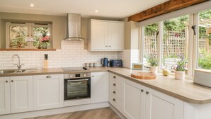 Une cuisine moderne avec des meubles blancs, un four encastré et une fenêtre donnant sur un jardin.