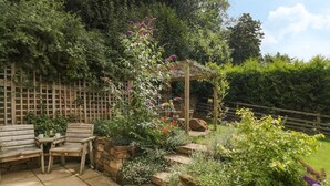 Une terrasse avec un sol en pierre, des meubles en bois et une variété de plantes et de fleurs.