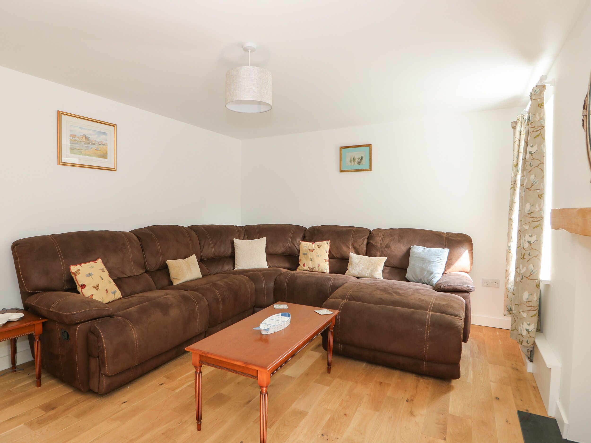 A living room with a brown sectional sofa, a wooden coffee table, and two framed pictures on the walls.