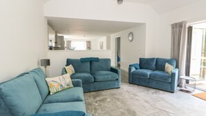 A spacious living room with two blue sofas, a coffee table, and a large mirror on the wall. - The Glass House (Hunstanton)