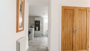 A hallway leading to a kitchen with a wooden door and a radiator on the wall. - The Glass House (Hunstanton)