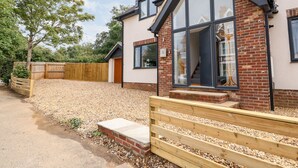 A modern house with a large glass window, a wooden deck, and a gravel driveway. - The Glass House (Hunstanton)