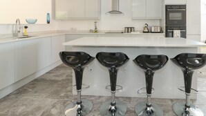 A modern kitchen with white cabinets, a central island, and three black bar stools. - The Glass House (Hunstanton)