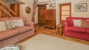 A cozy living room with two sofas, a wooden cabinet, a staircase, and a chandelier. - The Old Bakery (Taunton)