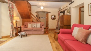 A cozy living room with a wooden staircase, a red sofa, a pink sofa, and a small table with a lamp. - The Old Bakery (Taunton)