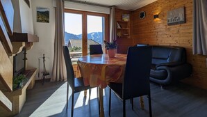 Una camera accogliente con arredamento in legno, un tavolo da pranzo con sedie, un divano e vista sulle montagne attraverso una grande finestra.