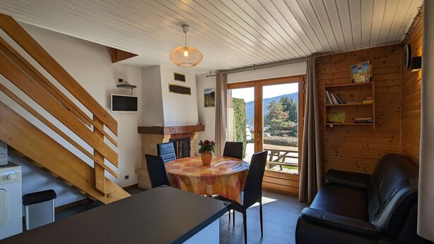 Un accogliente interno di una baita con zona pranzo, divano, scala e vista sull'esterno.