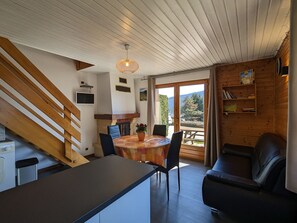 A cozy cabin interior with a dining area, a sofa, a staircase, and a view of the outdoors.