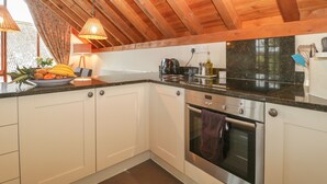 A kitchen with white cabinets, a black countertop, a stainless steel oven, and a wooden ceiling. - Flora's Barn (Taunton)