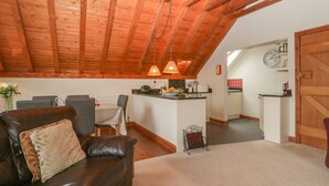 A cozy living room with a leather sofa, a dining table, and a kitchen in the background. - Flora's Barn (Taunton)
