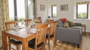A dining area with a wooden table and chairs, a grey sofa, and a window with a view of greenery. - Enzie Station Cottage (Buckie)