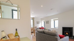 A living room with a sofa, a fireplace, and a dining area with chairs. - Enzie Station Cottage (Buckie)
