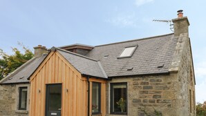 A stone house with a wooden extension, a sloped roof, and a chimney. - Enzie Station Cottage (Buckie)