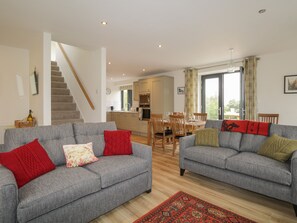 A modern living room with two grey sofas, a wooden staircase, a kitchen in the background, and a dining area. - Enzie Station Cottage (Buckie)