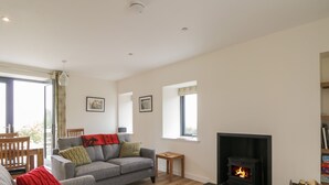 A modern living room with a grey sofa, red cushions, a patterned rug, a fireplace, and a bookshelf. - Enzie Station Cottage (Buckie)