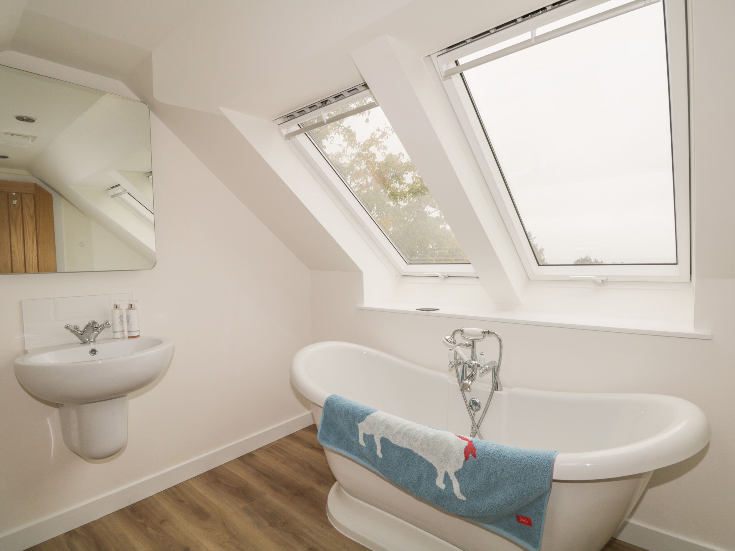 A modern bathroom with a skylight, a freestanding bathtub, and a pedestal sink.