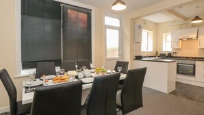 A modern kitchen with white cabinets, a central island, and a dining area with black chairs and a table set for a meal. - St. Heliers (Blackpool)