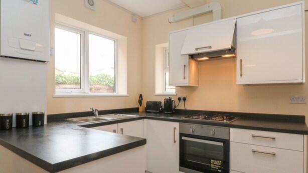 A modern kitchen with a gas stove, oven, and sink. There are cabinets and a window providing natural light. - St. Heliers (Blackpool)