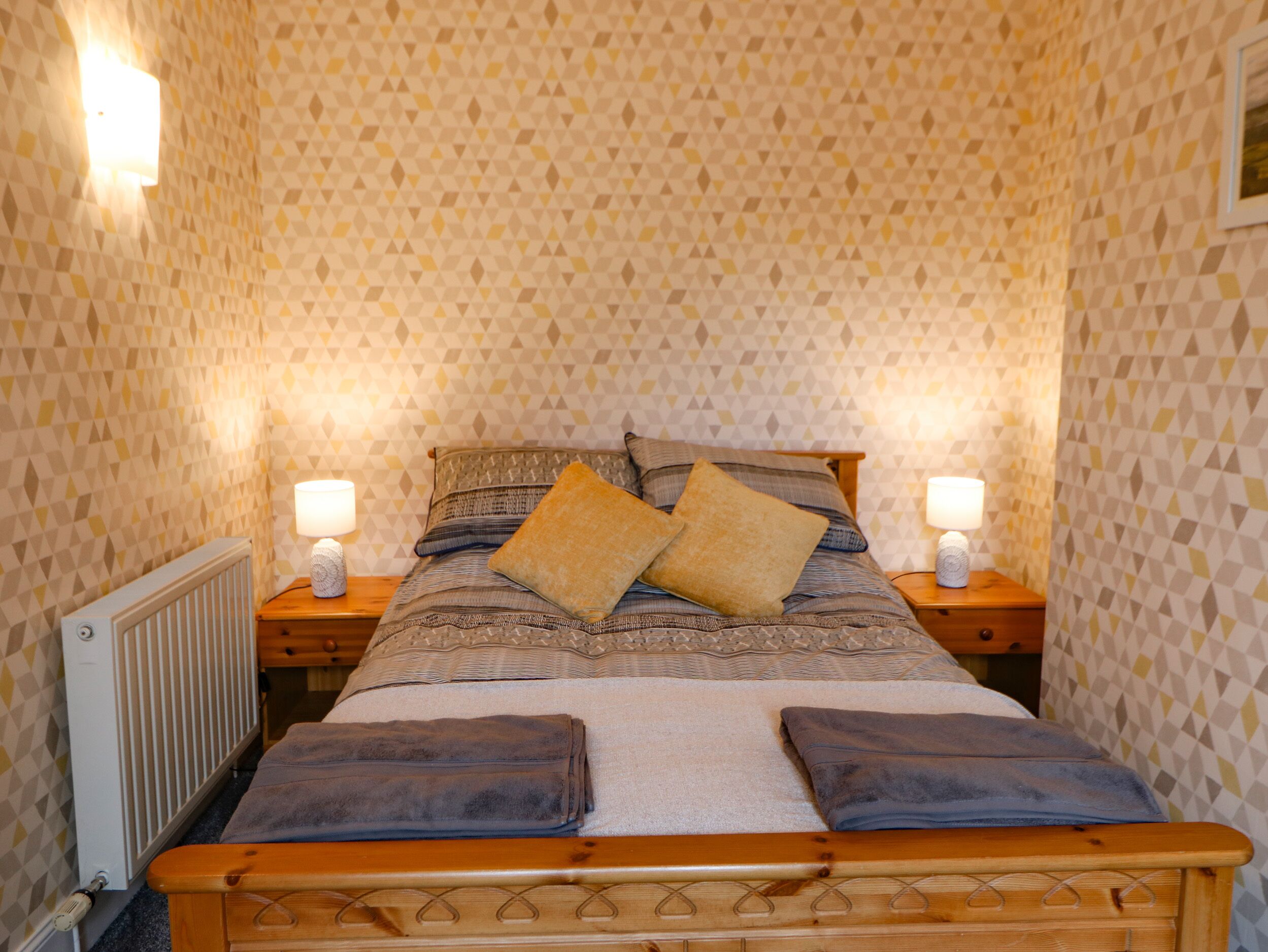 A neatly made bed with two pillows, a bedside lamp, and a wooden headboard.