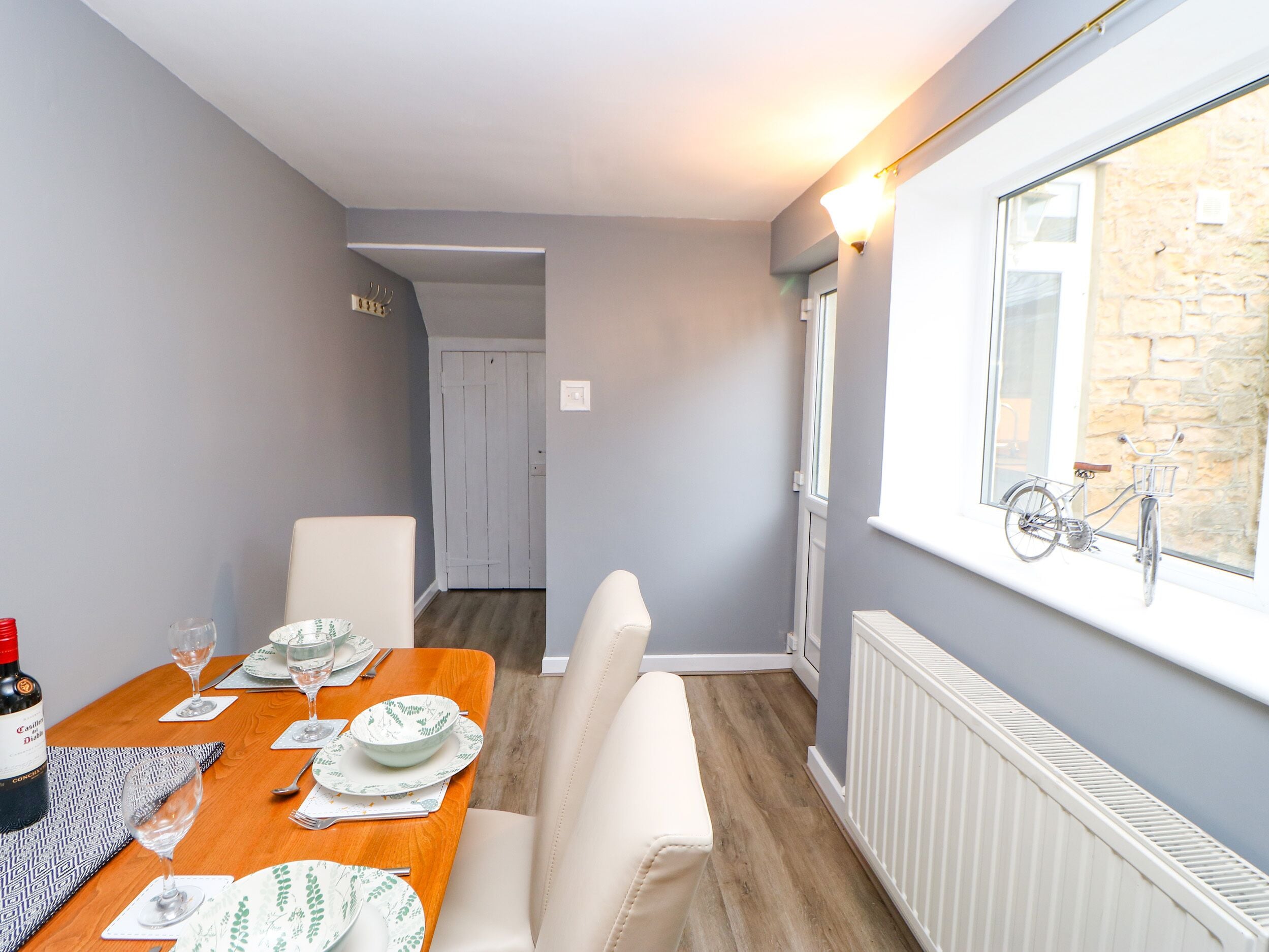 A dining area with a wooden table set for two, a white chair, and a radiator on the wall.