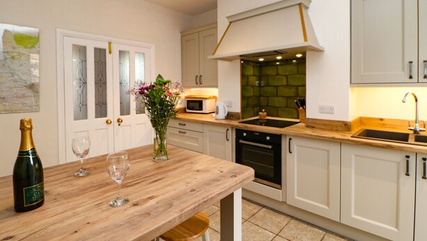 A modern kitchen with white cabinetry, a wooden dining table, and a green backsplash. - Stang View (Barnard Castle)