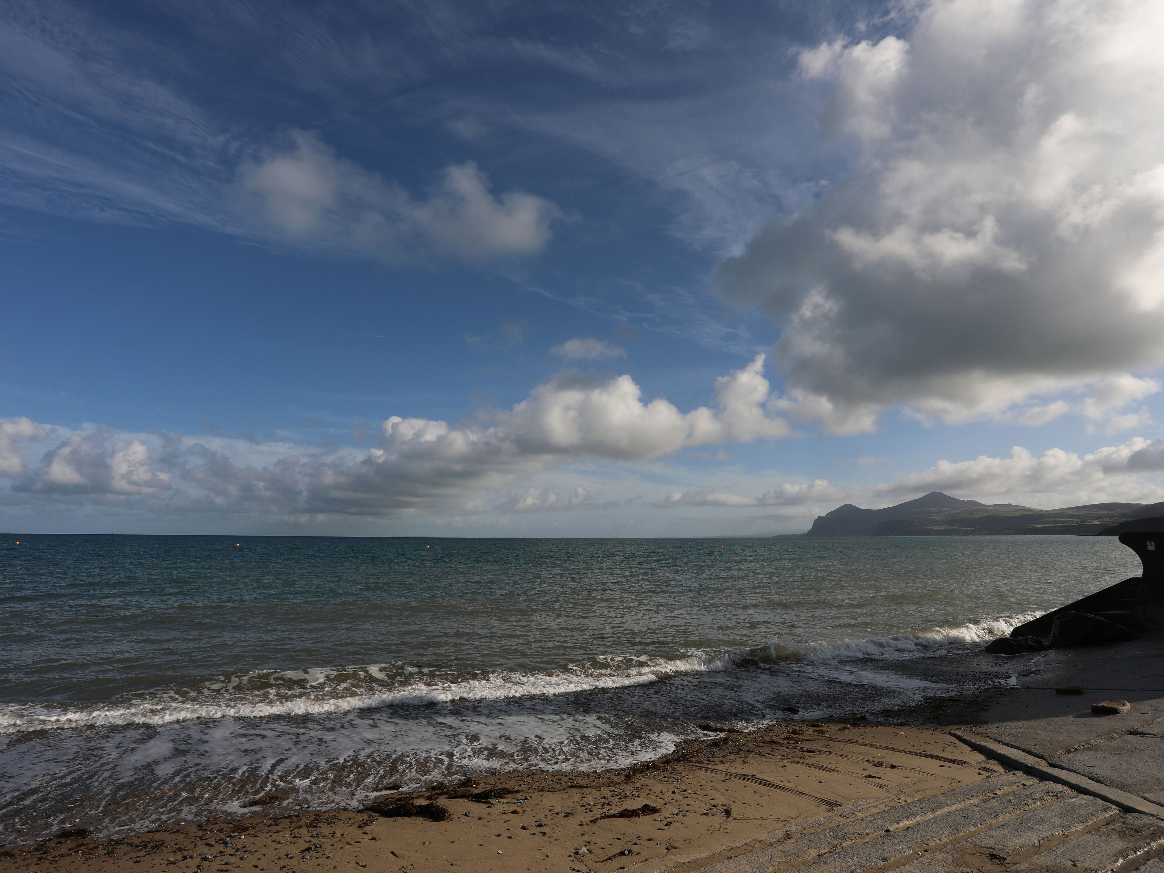 Uma praia com céu claro, ondas e montanhas ao longe.