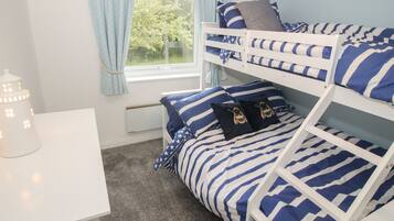A bunk bed with blue and white striped bedding, a small white desk, and a window with light blue curtains.