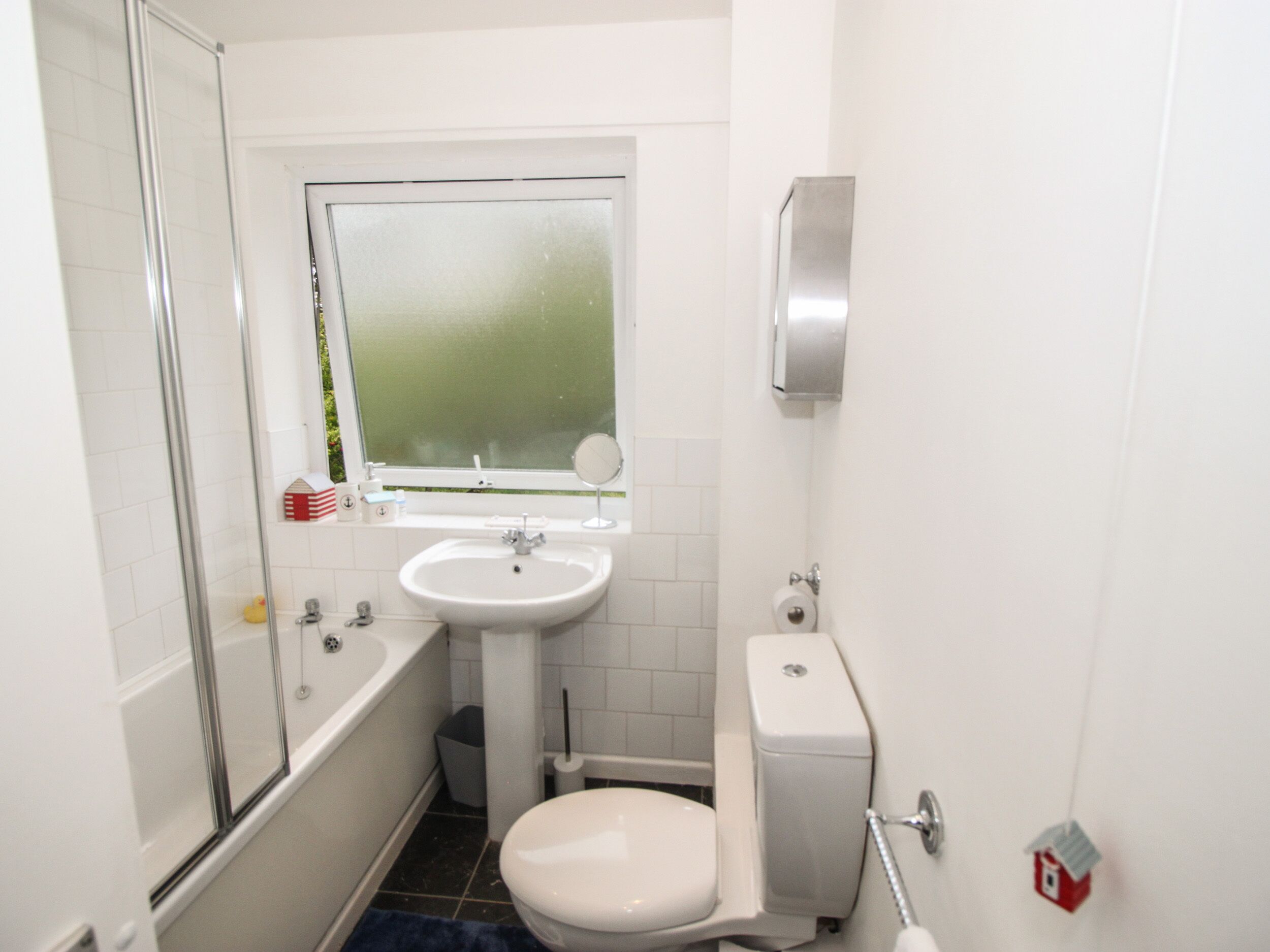 A compact bathroom with a shower, sink, toilet, and a small window.