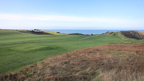 Un paisaje costero con un campo de golf, una carretera y una vista distante del mar.