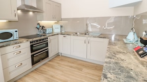 A modern kitchen with white cabinets, a microwave, a toaster, and a sink. - Y Stabl (Llanrwst)