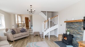 A spacious living room with a sofa, a fireplace, a staircase, and a chandelier. - Y Stabl (Llanrwst)