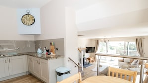 A modern kitchen with white cabinets, a marble countertop, and a clock on the wall. - Y Stabl (Llanrwst)