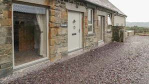 A stone building with a gravel driveway and a wooden fence. - Y Stabl (Llanrwst)