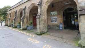 A historic stone building with arched doorways and a red door. There are potted plants at the entrance and a sign on the wall. - Jasmine Cottage (Richmond)