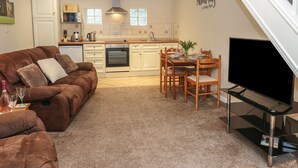 A modern living room with a brown leather sofa, a dining table with chairs, a flat-screen TV, and a kitchen in the background. - Jasmine Cottage (Richmond)