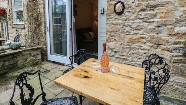 A stone building with a wooden table and chairs, a bottle, and a glass. - Jasmine Cottage (Richmond)